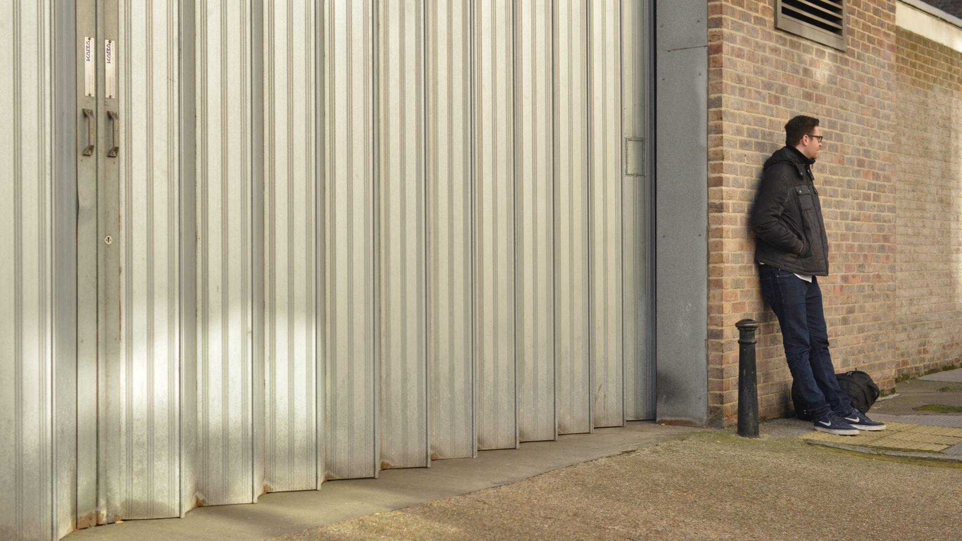 Man standing outside of prison, leaning against brick wall