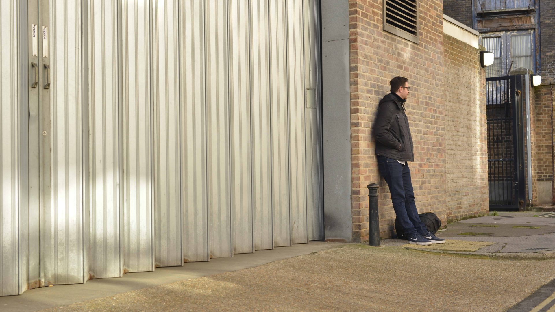 Man standing outside of prison, leaning against brick wall