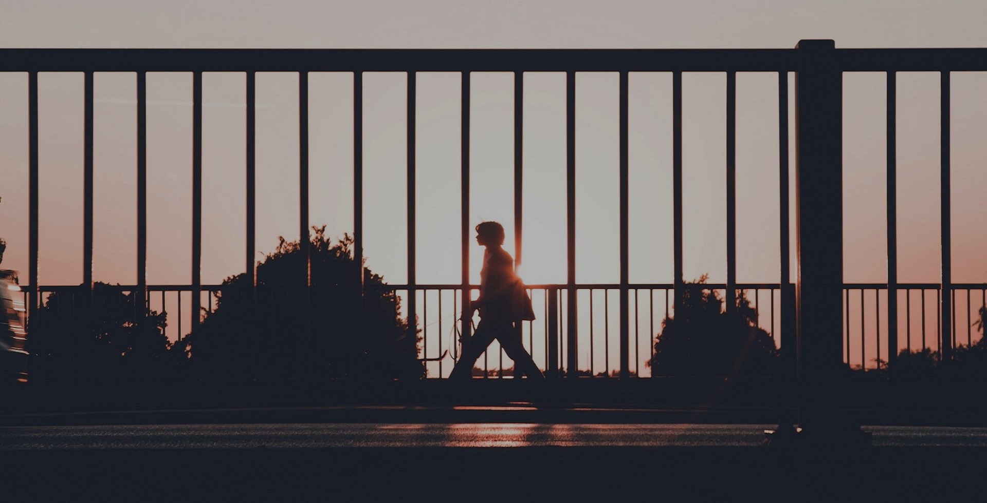 Photograph of someone walking past a gate at sunset