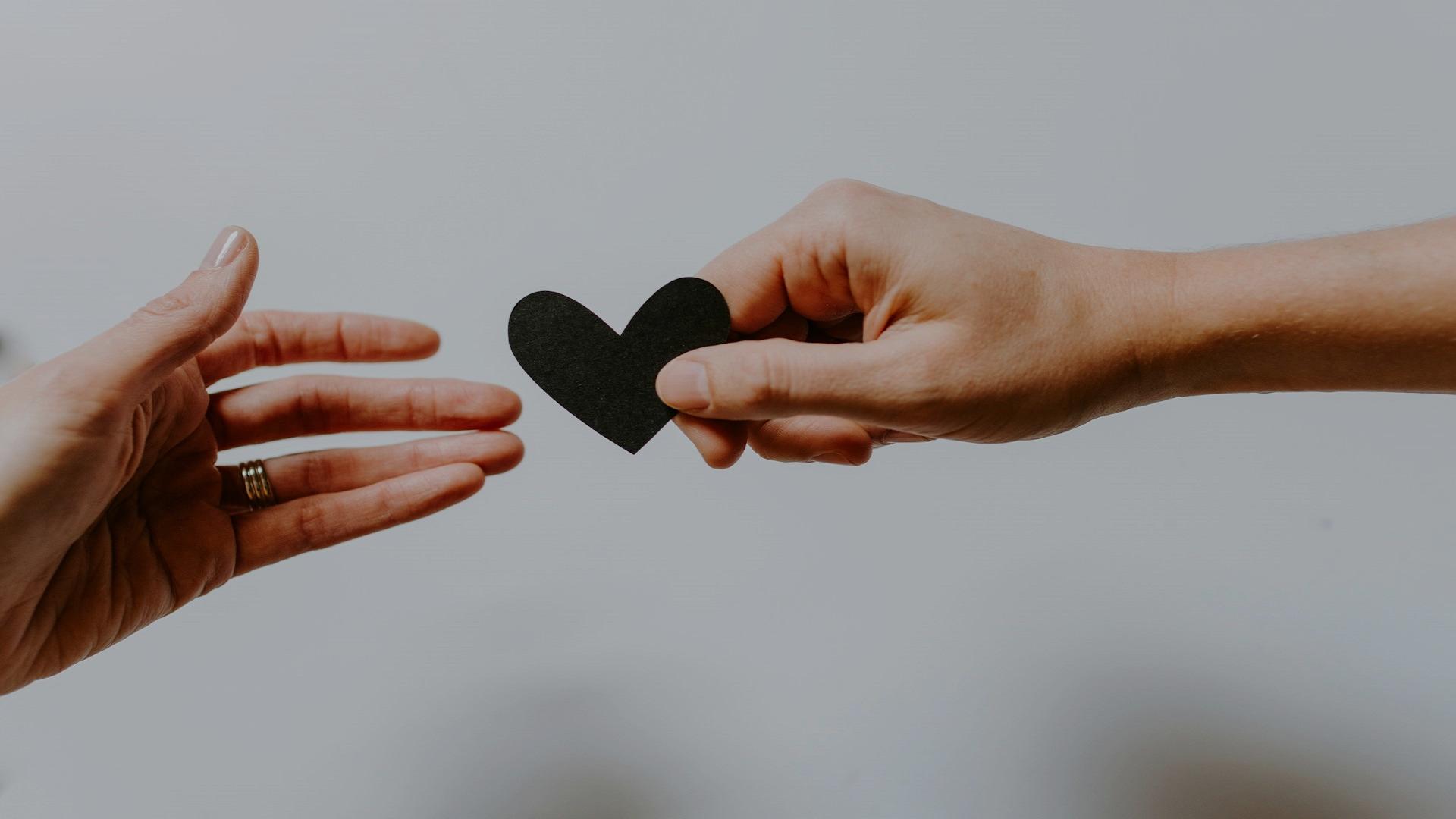 Image of a hand giving a cut out black heart to another hand